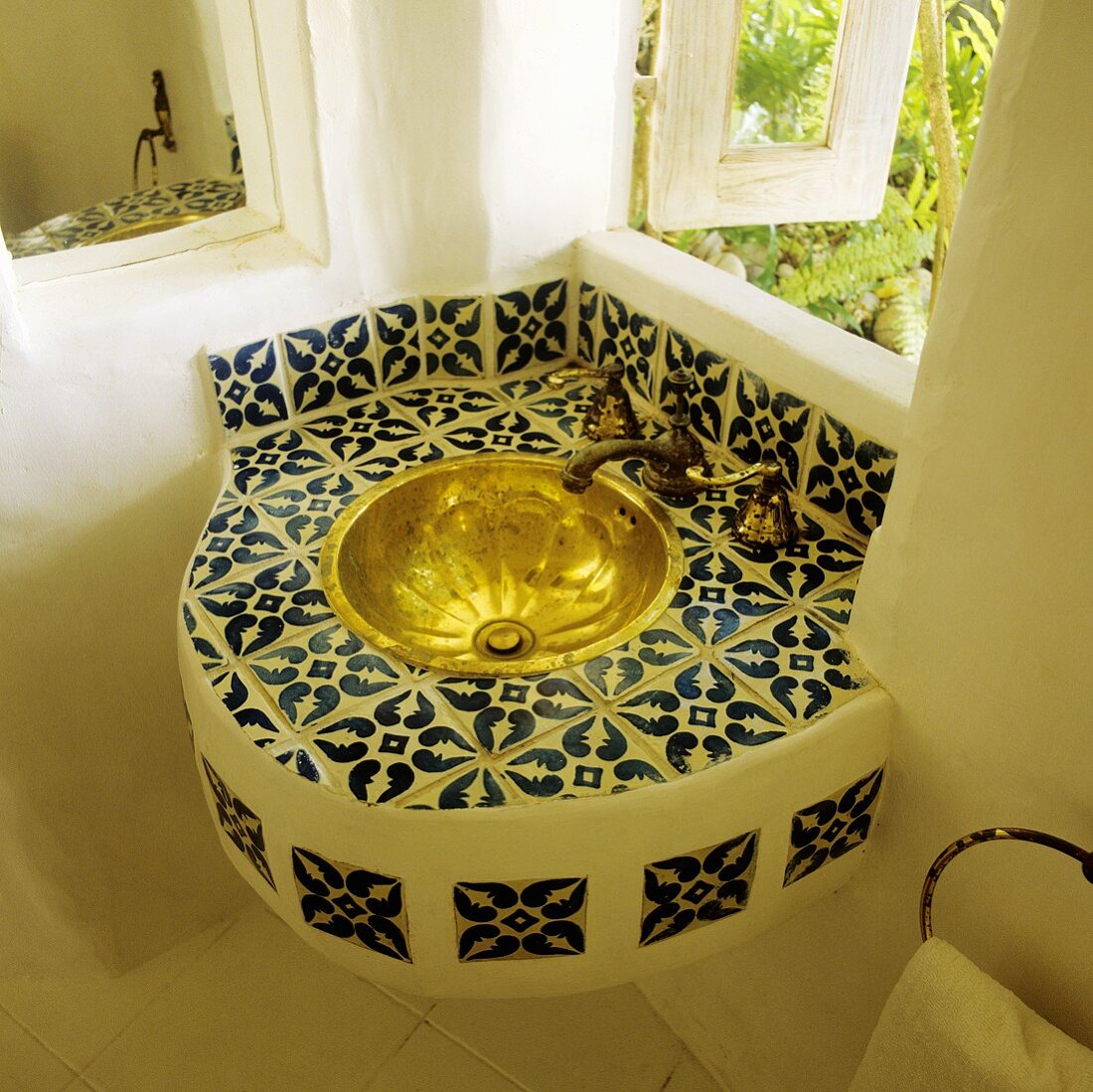 A corner of a bathroom with a tiled wash basin and a brass basin