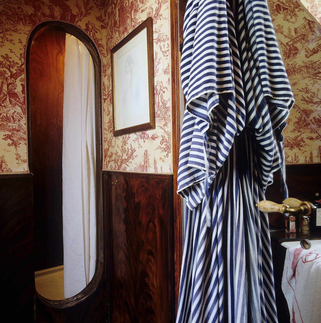 Bad mit gemusterter Tapete auf Wand und gestreifter Bademantel hängend neben Türöffnung der Duschkabine