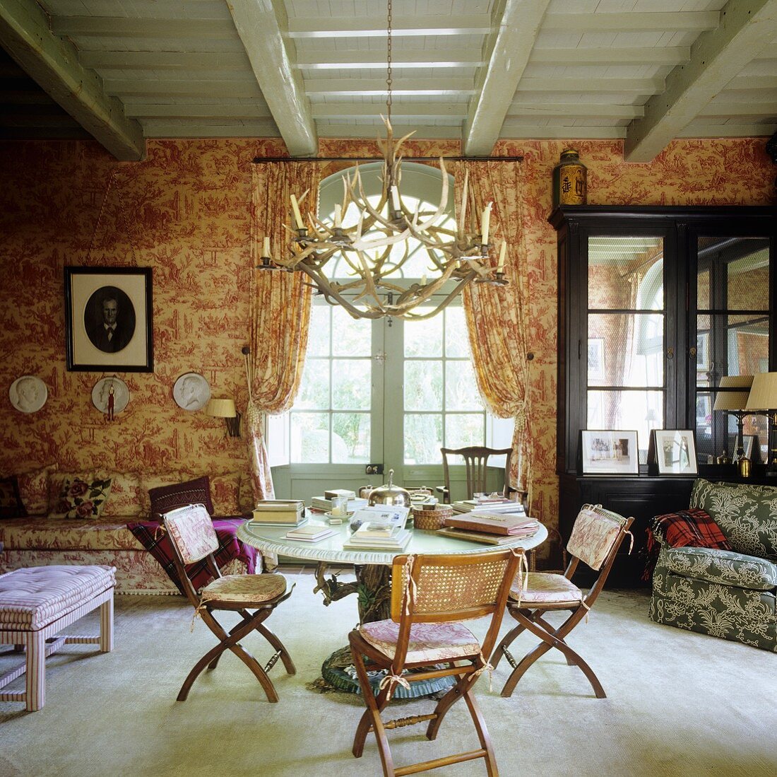 Wohnraum mit Steintisch und Hirschgeweihleuchter an grauer Holzdecke im französischen Landhaus