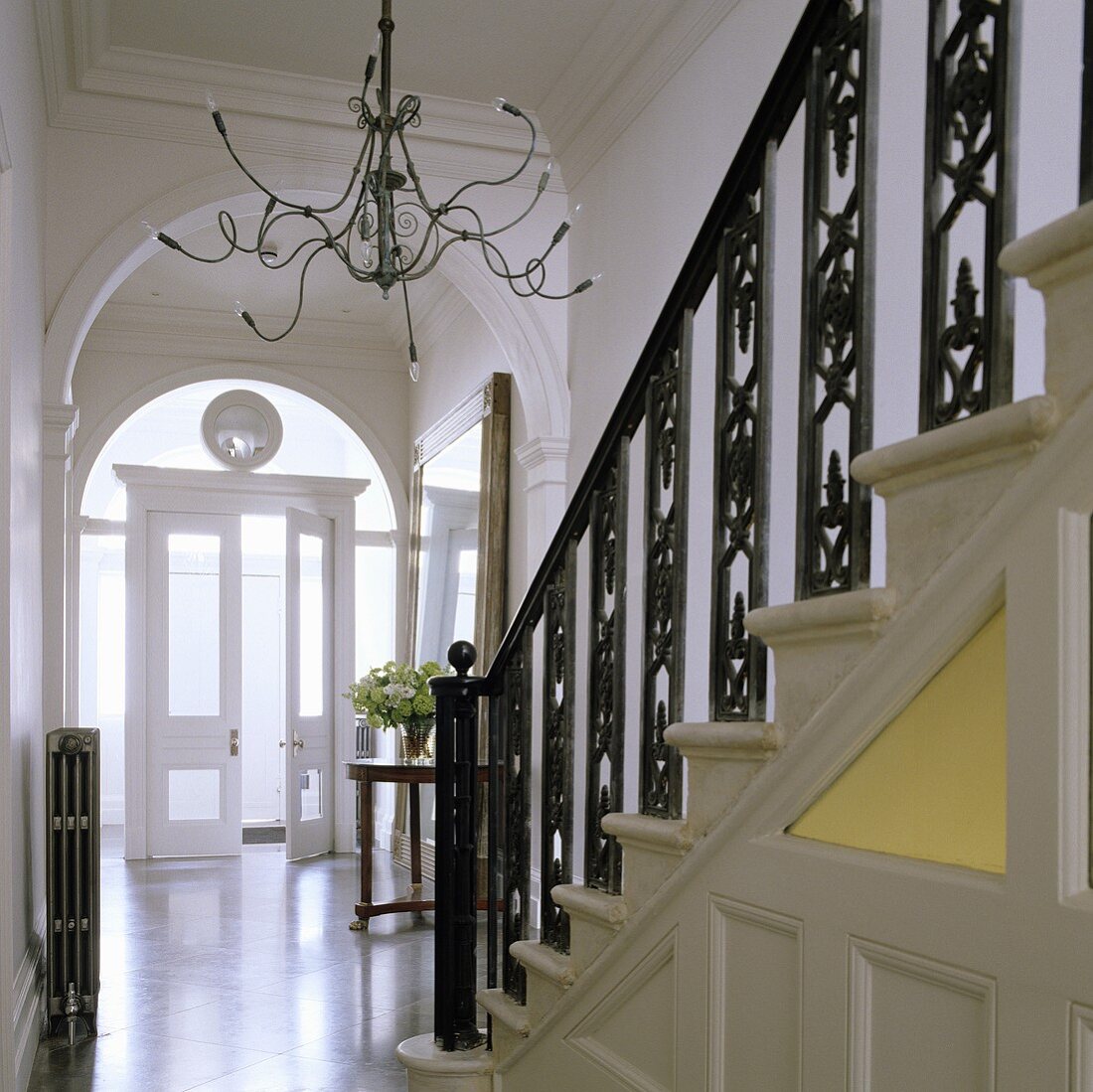 Treppenaufgang mit schwarzem schmiedeeisernem Geländer und Kerzenleuchter mit Medusaarmen vor Rundbogen
