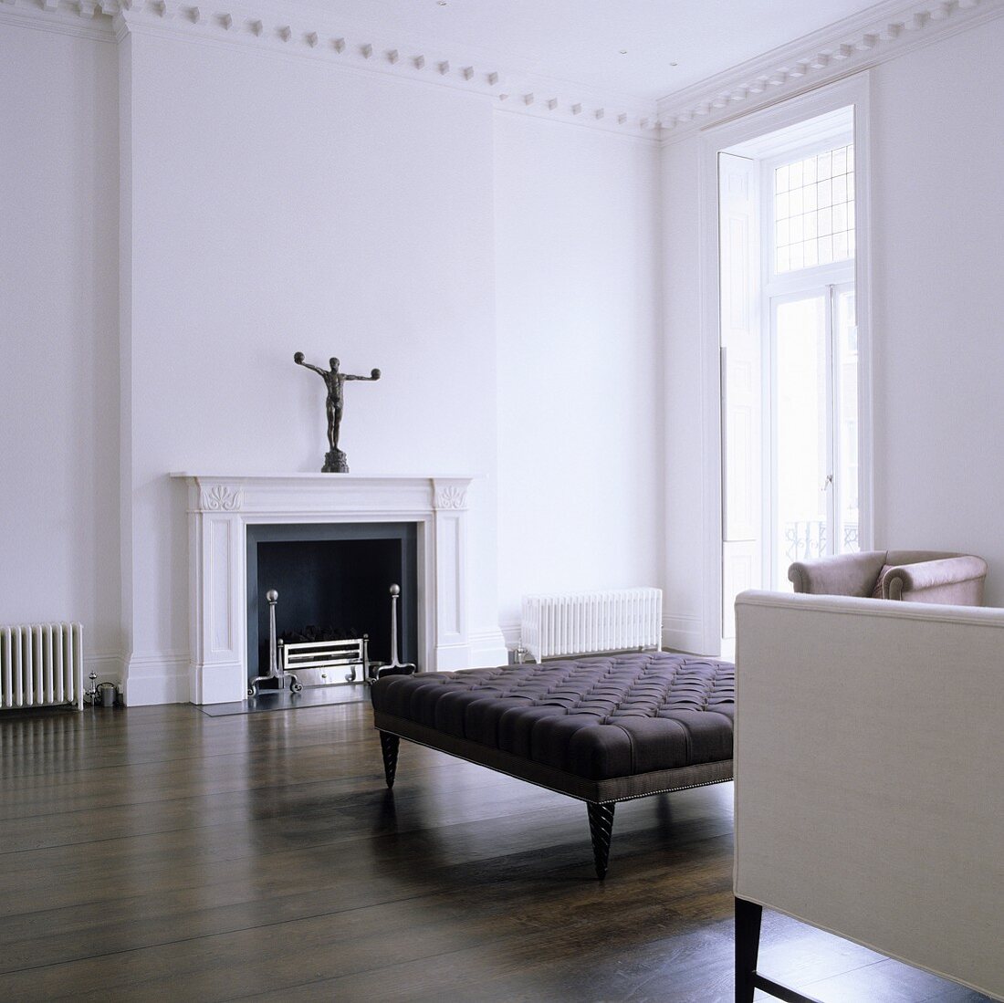 A minimalistic living room with an antique sofa on dark wooden floorboards in front of a fireplace