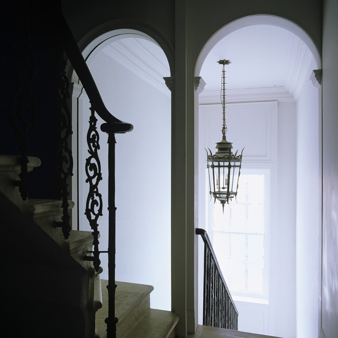 A white-painted stairway with archways and a view of a ceiling lantern