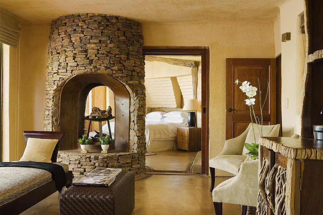 A natural stone fireplace in a yellow-painted living room with a view into a bedroom in a South African house