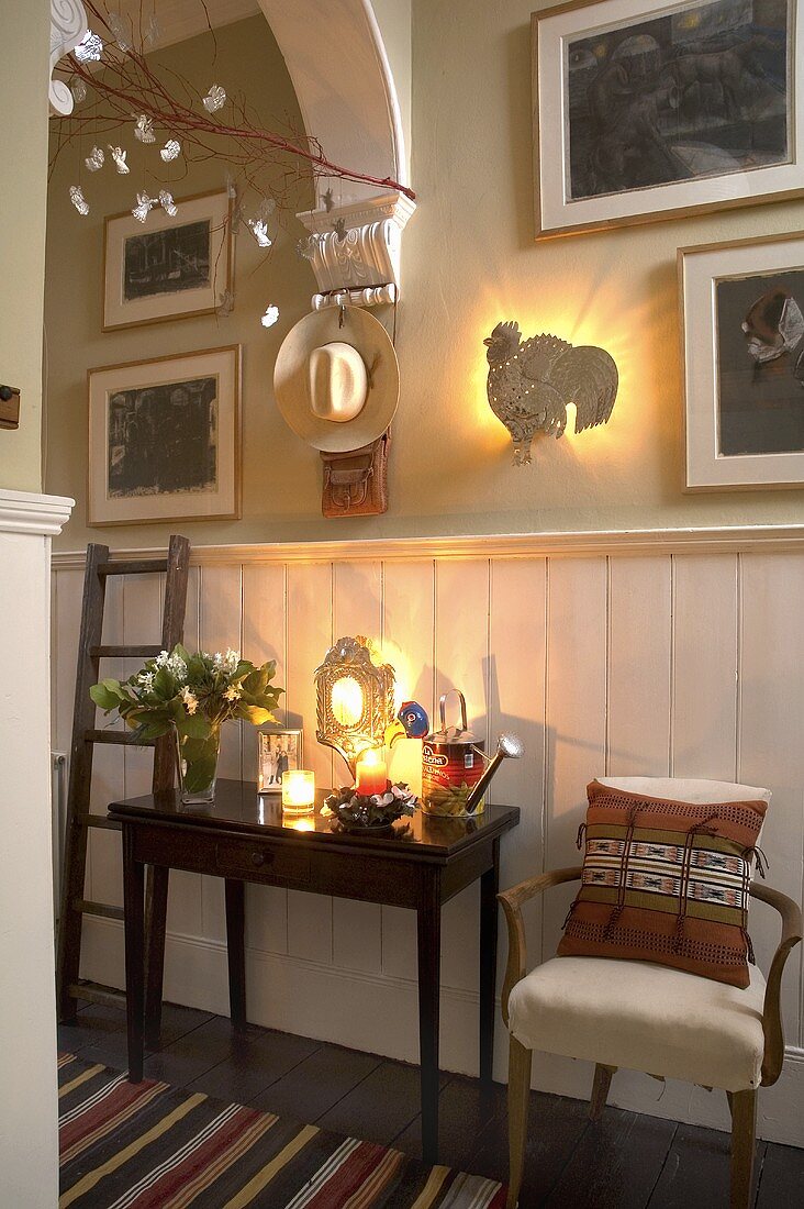 An antique wall table and an armchair in front of white wood panelling in a hallway