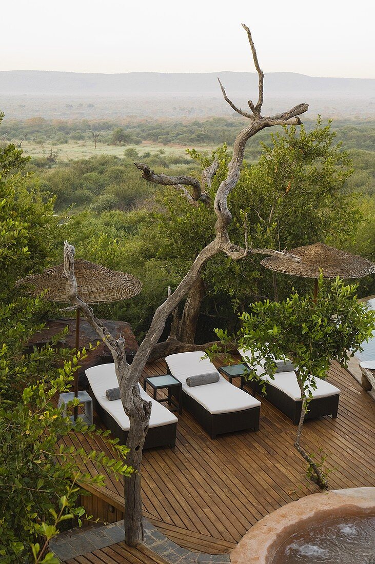 Liegestühle auf Holzterrasse mit Bambusschirmen und Blick auf die südafrikanische Landschaft