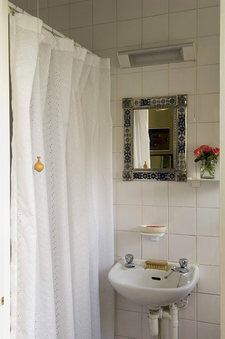 Waschbecken mit Spiegel an weiss gefliester Wand und geschlossener Duschvorhang