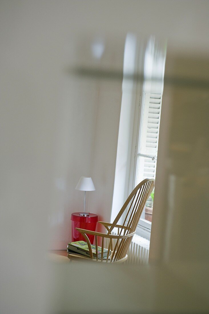 Blick durch Fensterausschnitt auf Sprossenrückenlehne eines Holzstuhls mit rotem Kunststoff- Beistelltisch