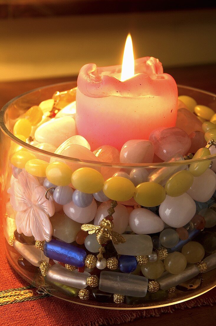 A glass container filled with a colourful beaded necklace and a burning candle