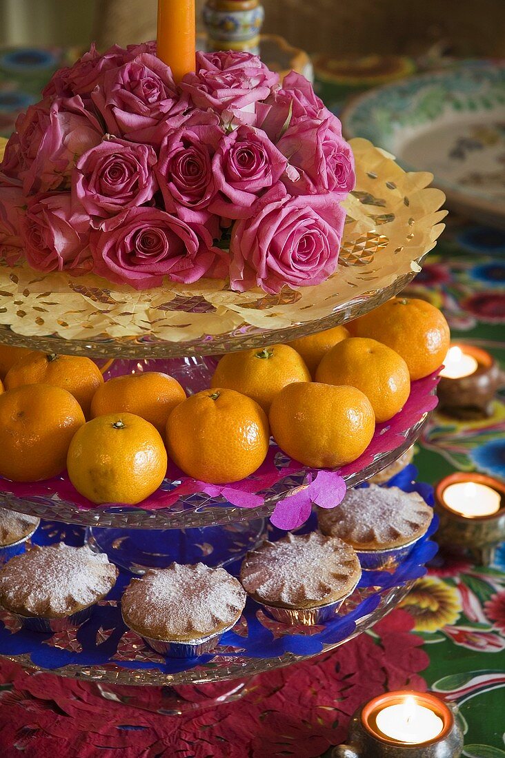 A cake stand with roses, mandarins, cakes and tea lights