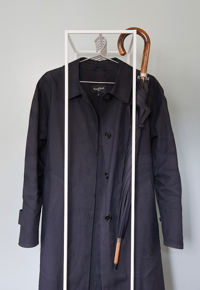 A black coat and an umbrella on a metal clothes stand