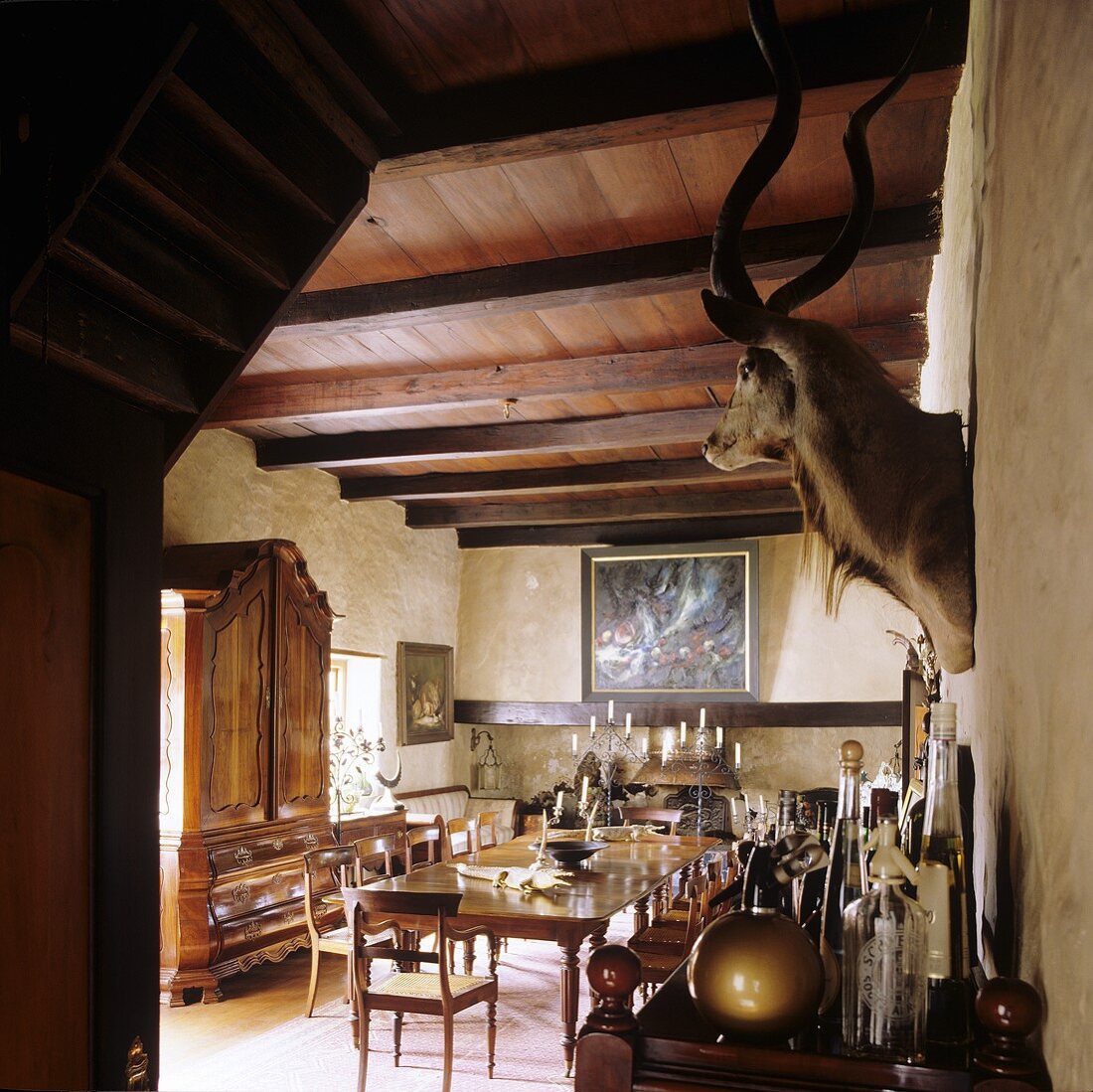 A dining room in a South African country house - an antique dining table, a wood beam ceiling and a stuffed animal head on the wall