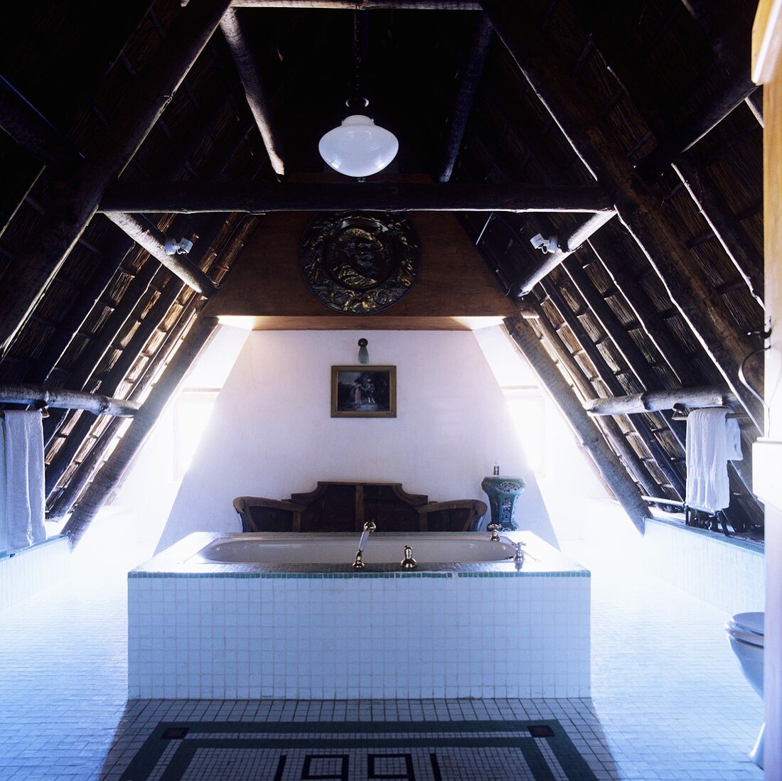 Bad im südafrikanischen Landhaus - weiße Badewanne in Raummitte unter Dachstuhl mit dramatischer Lichtinszenierung