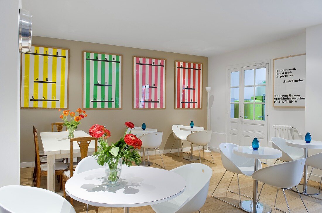 Bar tables and white bucket chairs in a hotel breakfast room with colourful posters on the grey wall