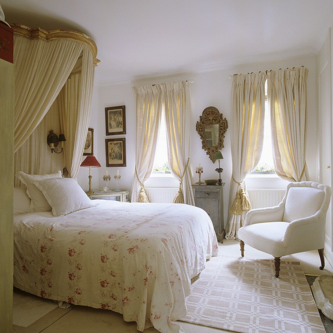 A double bed with a canopy and an antique armchair in a white bedroom