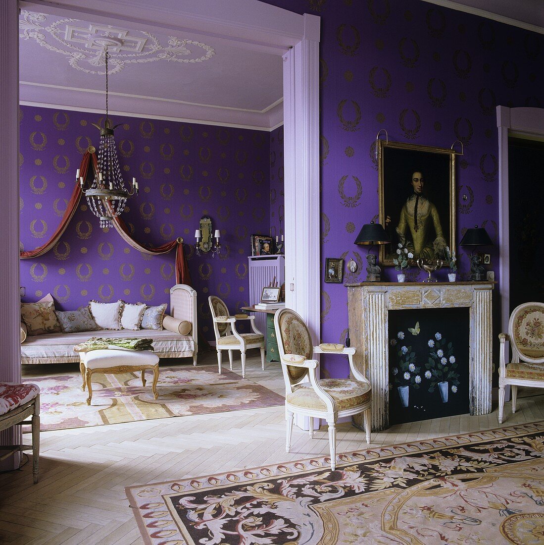 A fireplace room with an open doorway into a living room with purple wallpaper with a gold pattern