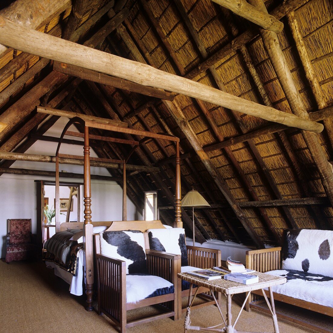 Schlafraum mit Holzstühlen und Fellbezug unter Dachstuhl mit Strohbelag im südafrikanischen Landhaus