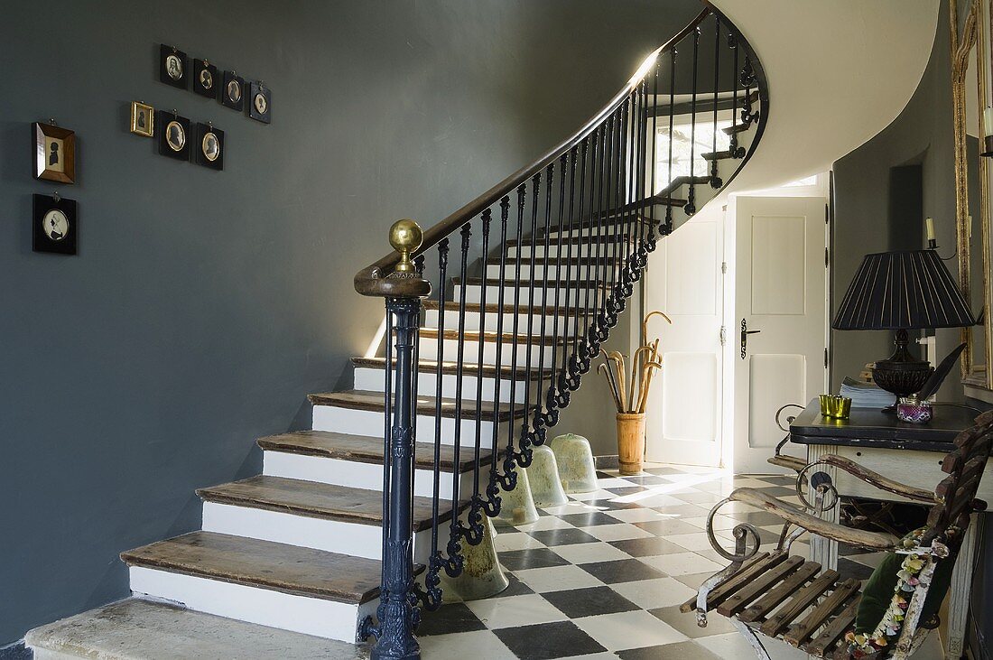 A flight of stairs with a dark grey wall and a black and white tiled floor in the hallway of a country house