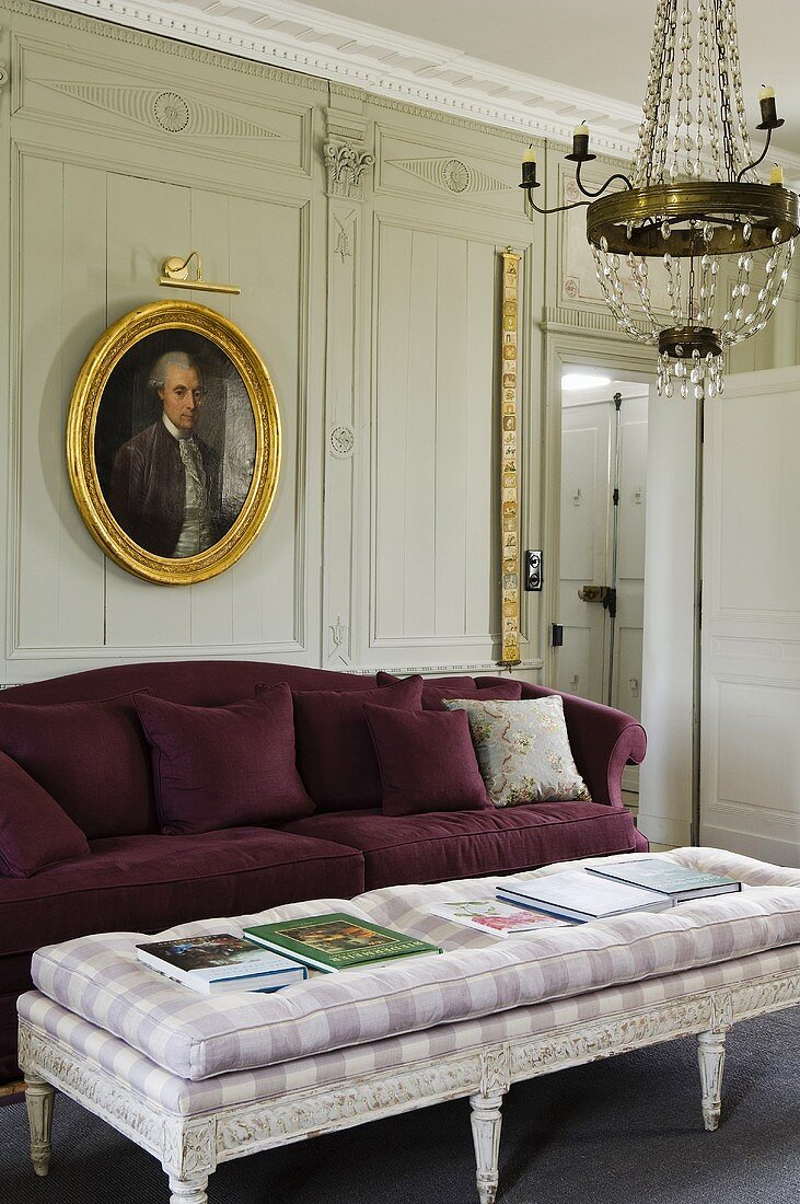 An upholstered Rococo-style coffee table with a purple two seater and a picture hanging on the wood panelled wall