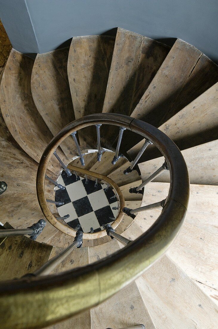 Stairwell of a spiral staircase drawing your attention down below to a checkerboard floor