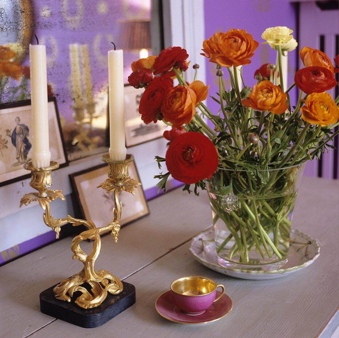 Rote Blumen in Glasvase und vergoldeter Kerzenständer neben Mokkatässchen auf der Holzablage