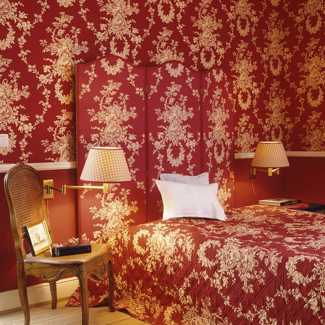 Schlafraum mit rot-weißem Blumen-Ornamentmuster auf Tapete, Paravent und Tagesdecke
