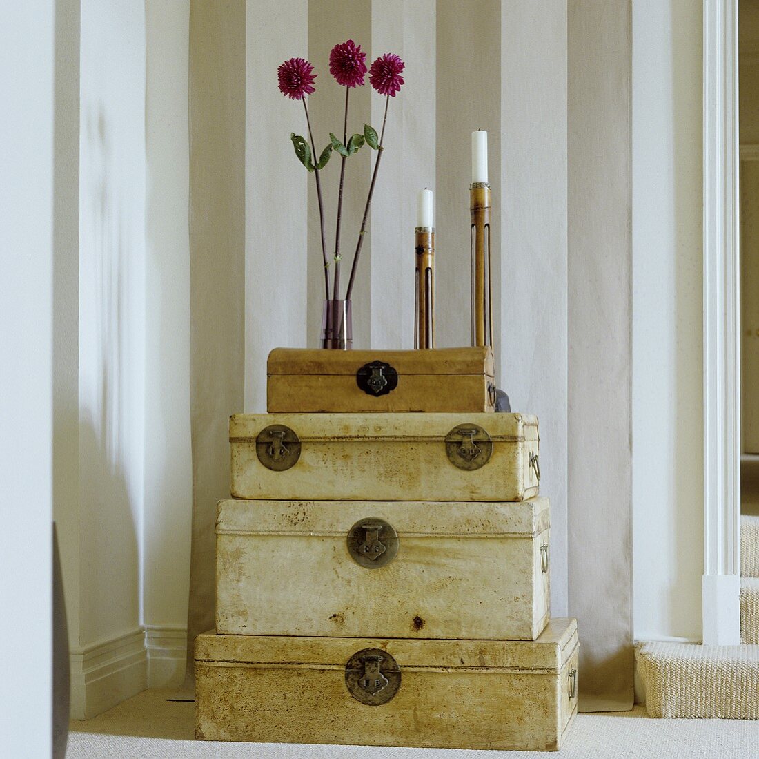A vase of flowers and a a candlestick on a stack of antique trunks against a striped wall