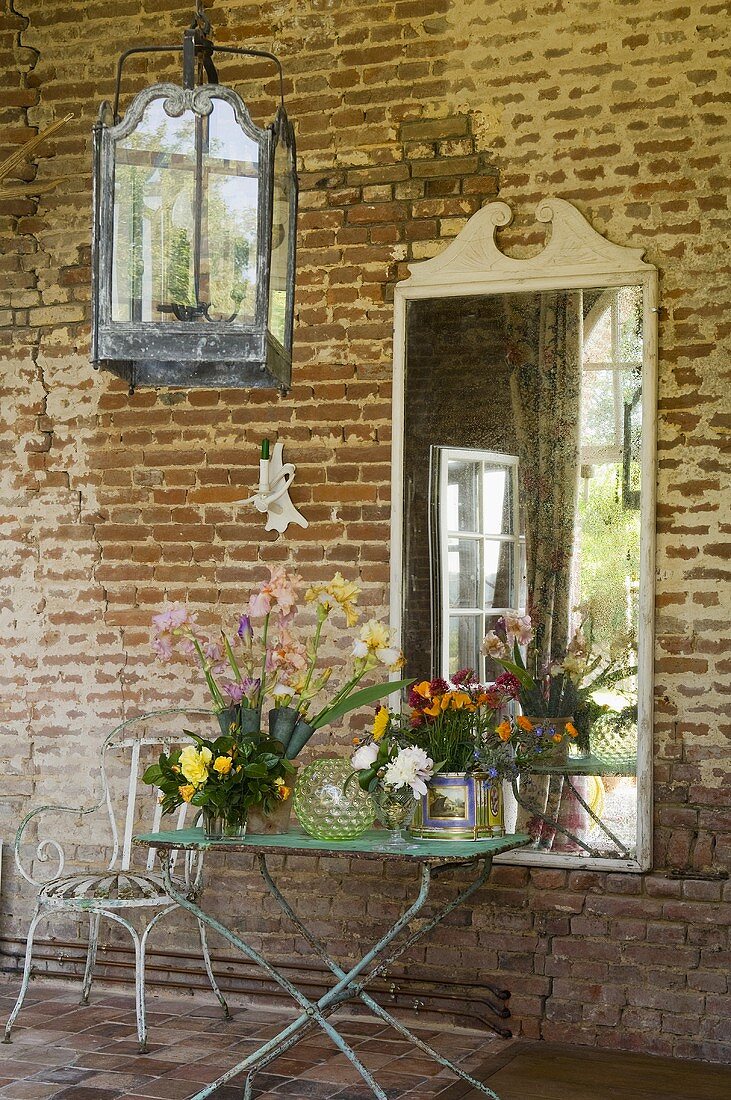 Gepflückte Gartenblumen auf Vintagetisch, Spiegel hängt an verwitterter Ziegelfassade