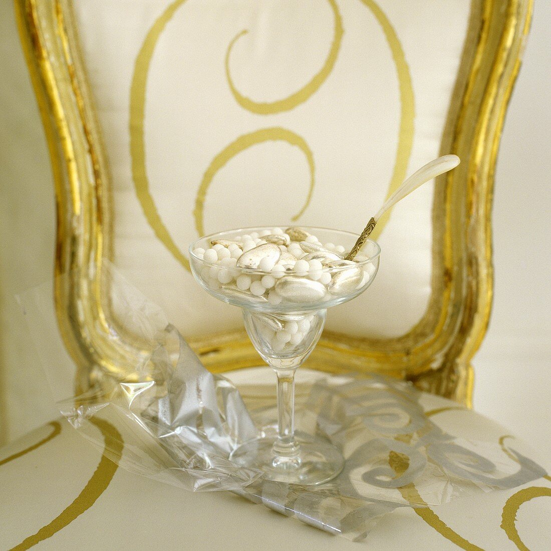 A spoon in a cocktail glass filled with beads and shells on a gold-framed chair