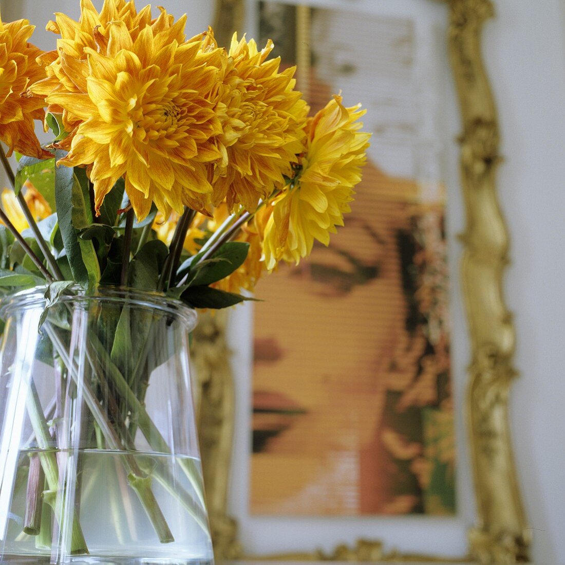 Gelbe Blumen in Glasvase und Frauenportrait an Wand