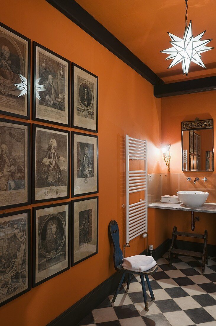 A gallery of ancestral portraits in a bright orange bathroom with a a black and white tiled floor