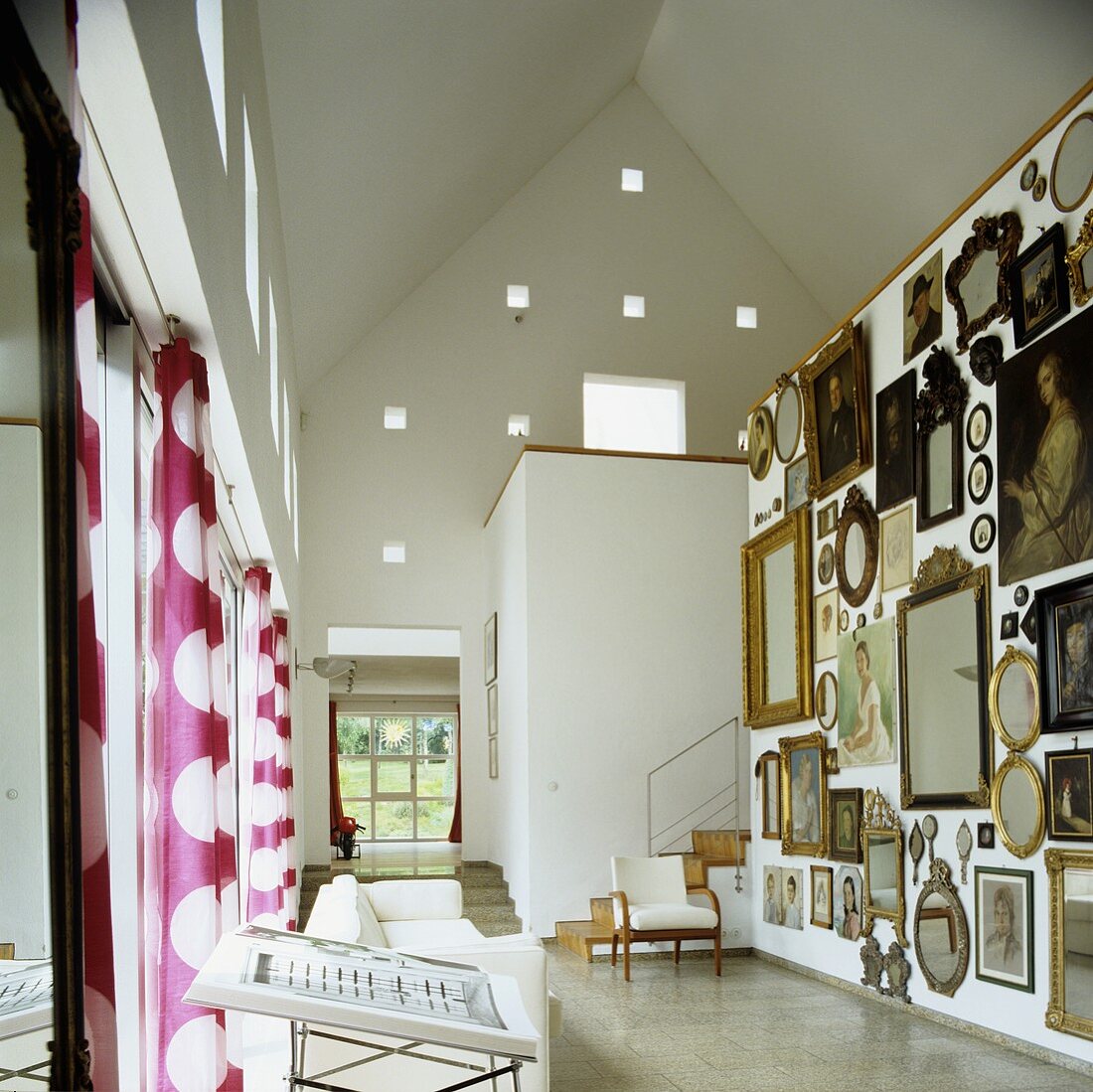 An open-plan living room with a collection of mirror on the wall and a window set into the gable wall