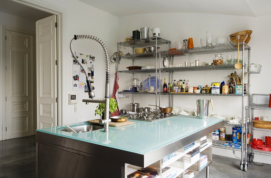 Coole Materialien - ausladender Küchenblock in Edelstahl mit Glasplatte vor offenem Regal