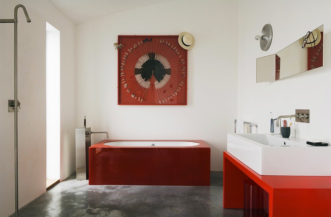 Minimalistisch designtes Bad - Waschbecken auf rotem Tisch und rote Glaswanne auf Betonboden