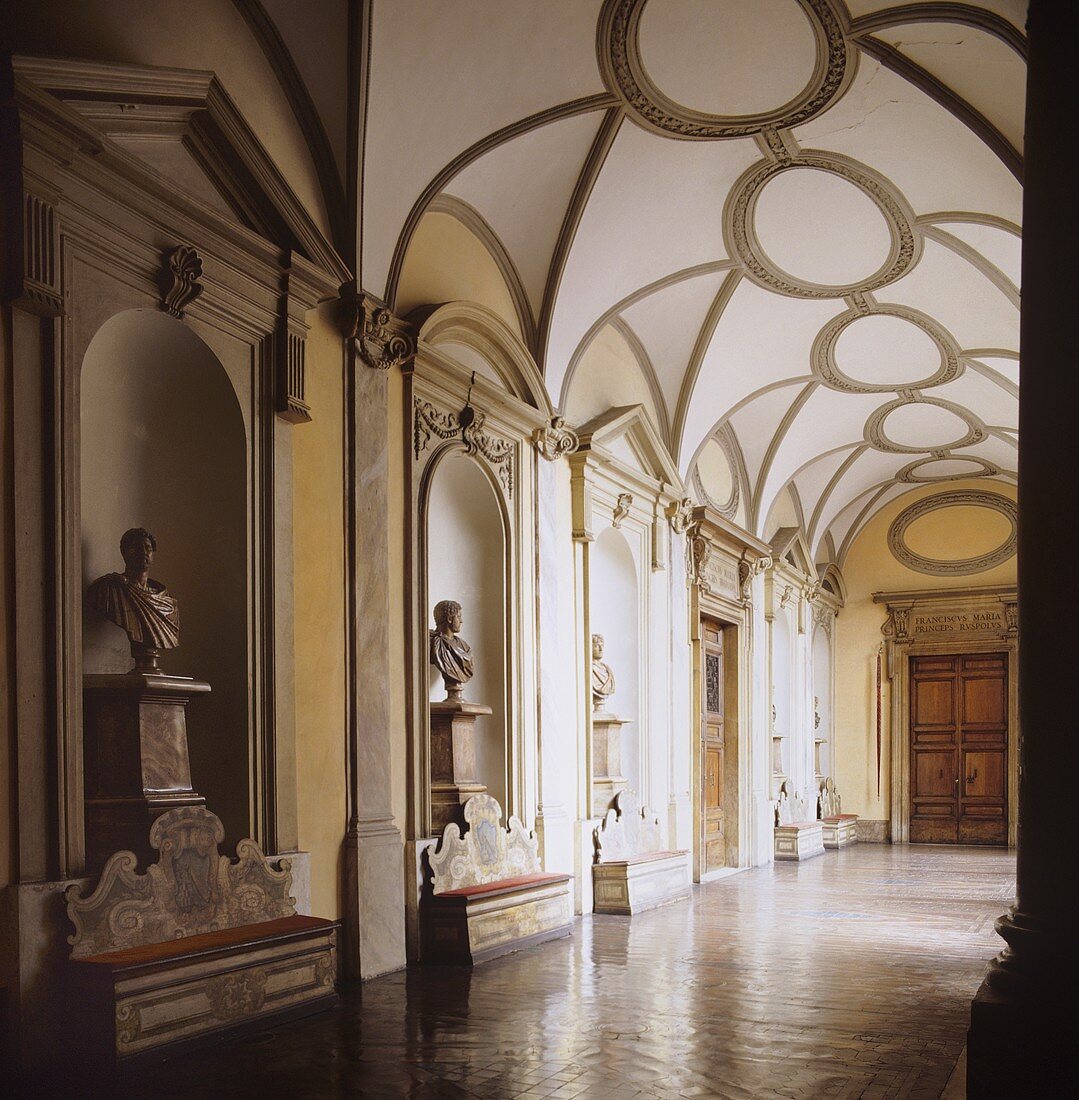 A hallway in a palazzo with busts in the wall niches and a vaulted ceiling