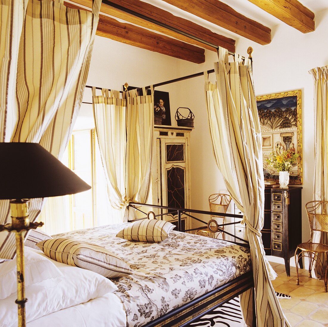 A delicate four poster bed under a rustic wood beam ceiling