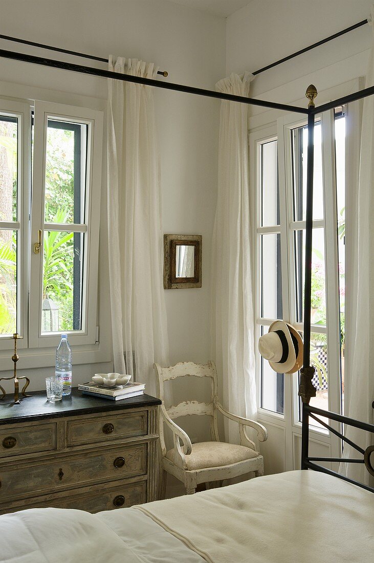 A vintage-style chest of drawers and a chair in the corner of a bedroom with a view