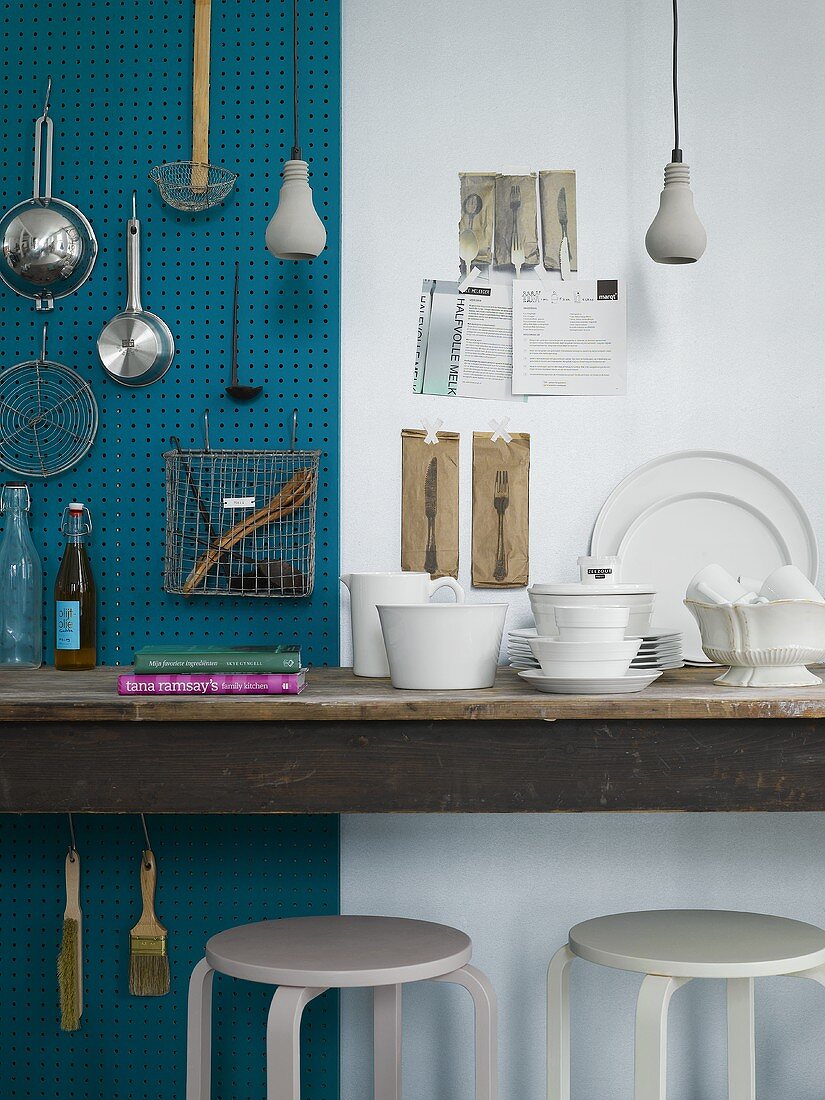 Stillleben aus gehängten Küchengeräten und weißem Designergeschirr auf Holztisch