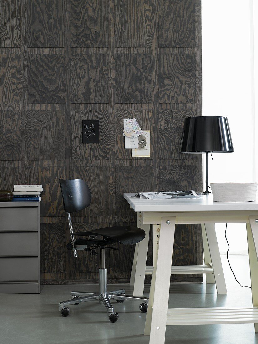 Schwarzweiss - weisser Schreibtisch mit schwarzem Bürostuhl vor dunkler holzvertäfelter Wand