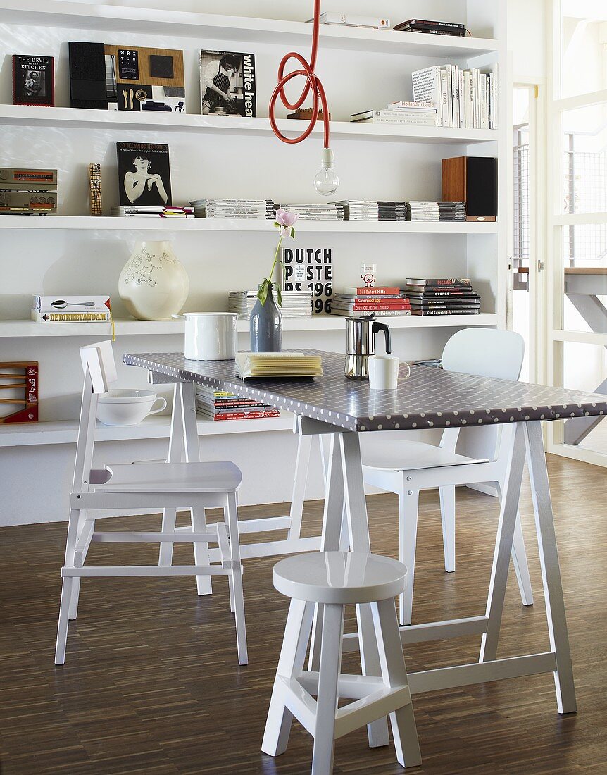 A coffee break on a trestle table with white chairs in front of a shelf