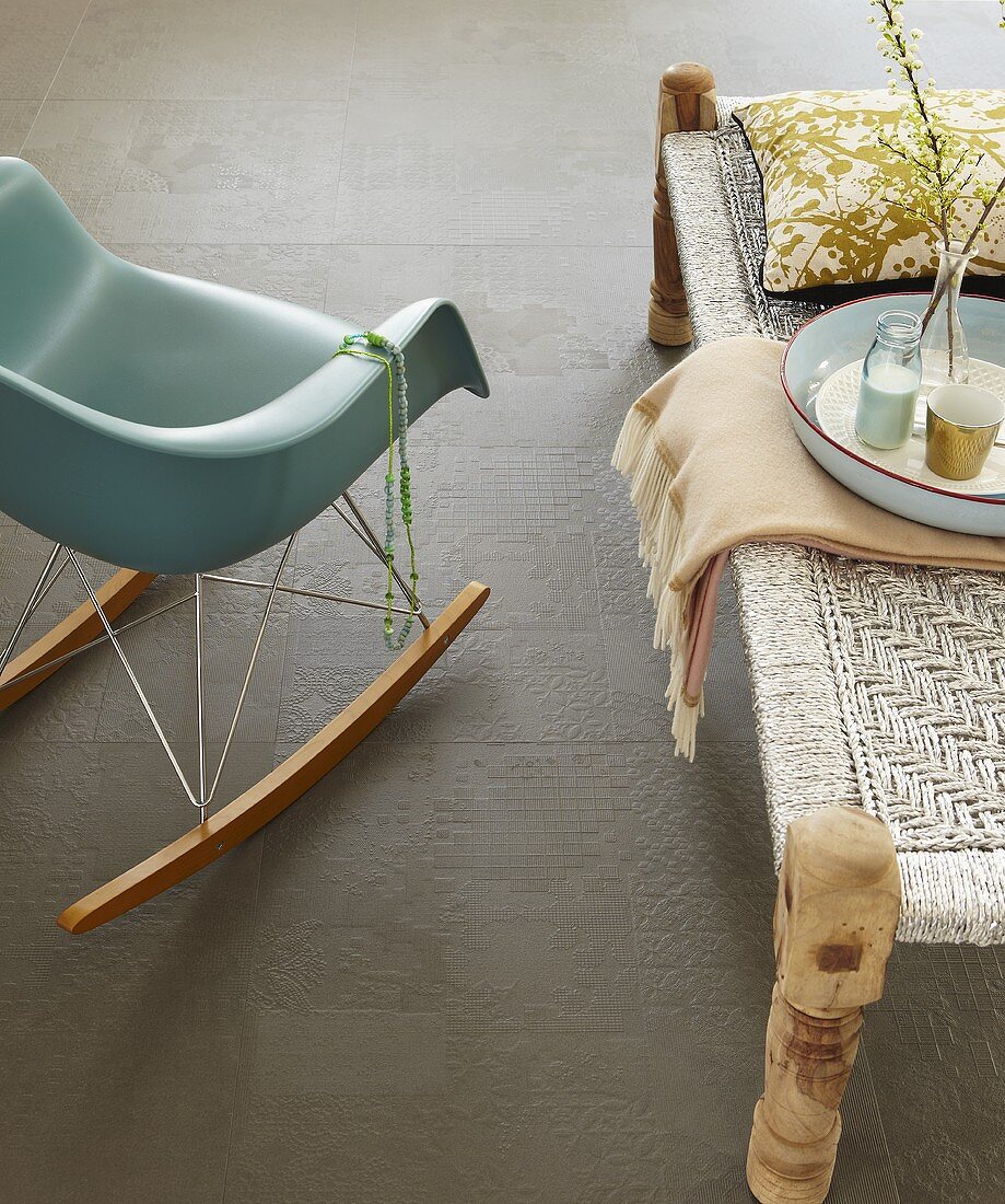 A rocking bucket chair next to a coffee table on a grey tiled floor