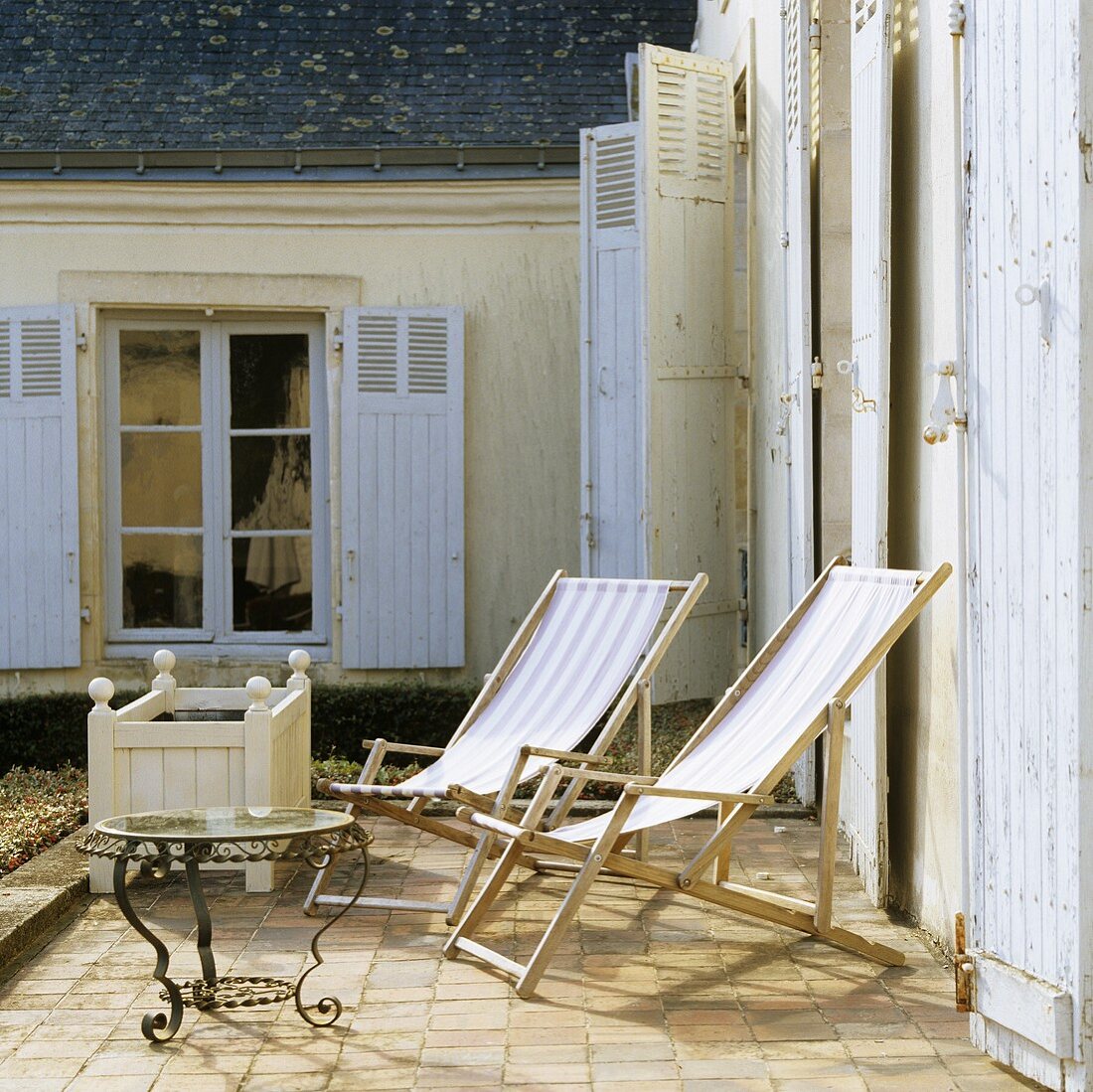 Erste Sonnenstrahlen auf der Terrasse - Holzliegestühle vor französischem Landhaus