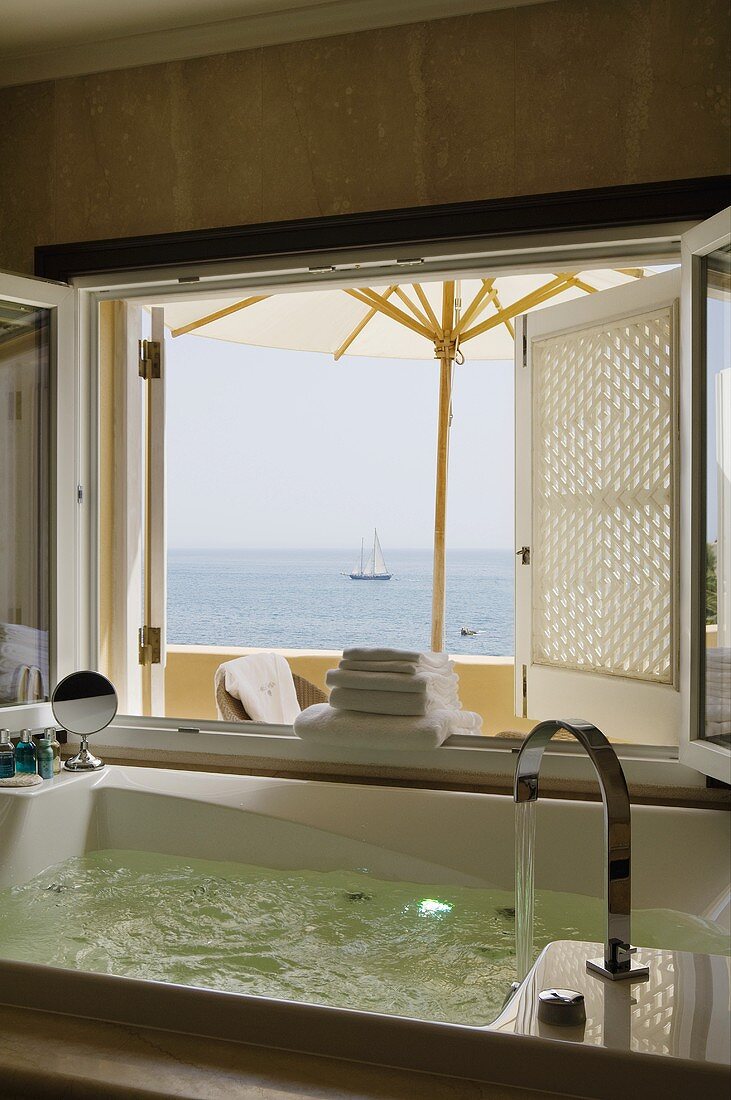 Eingelassener Whirlpool im Bad mit Blick durch geöffnetes Fenster auf Meer
