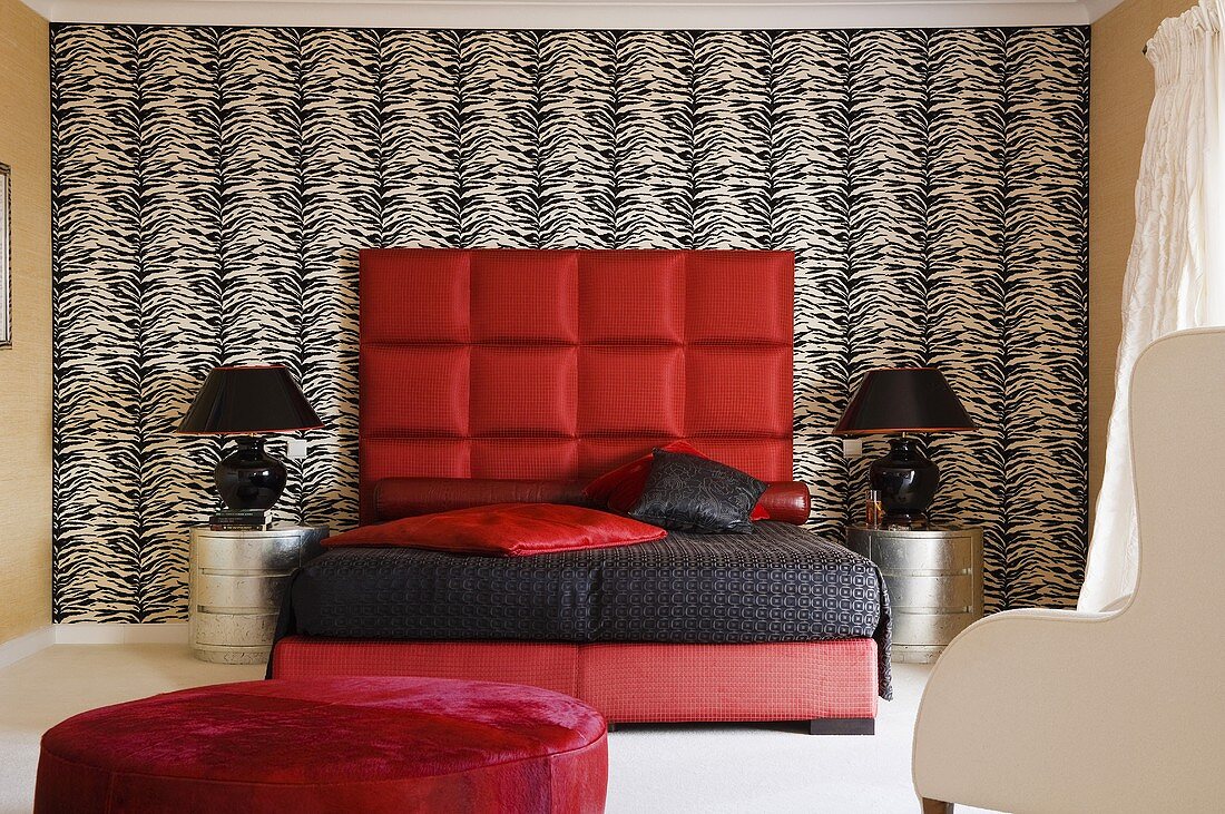 Peppiger Schlafraum - rotes Bett mit schwarzem Überzug und gepolstertem Kopfteil an schwarzweisser Wand