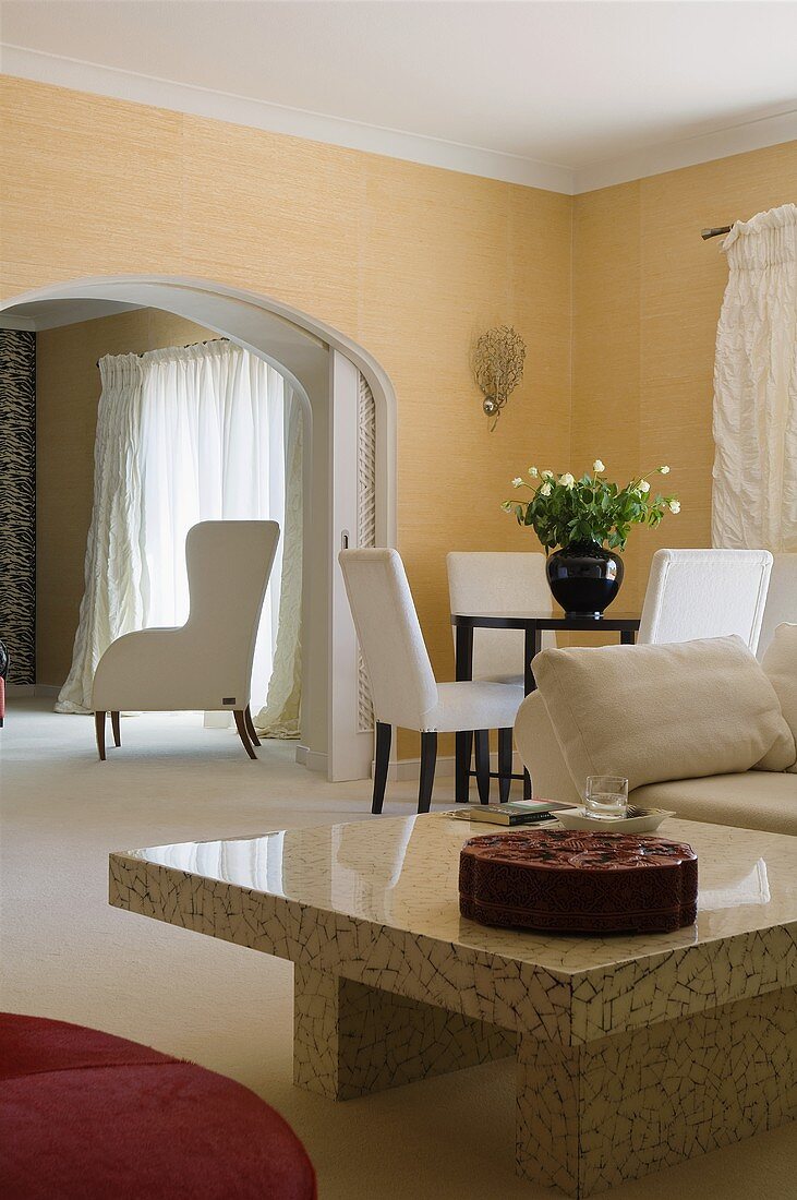 A shiny stone coffee table and a dining area with a view through a rounded archway of an armchair