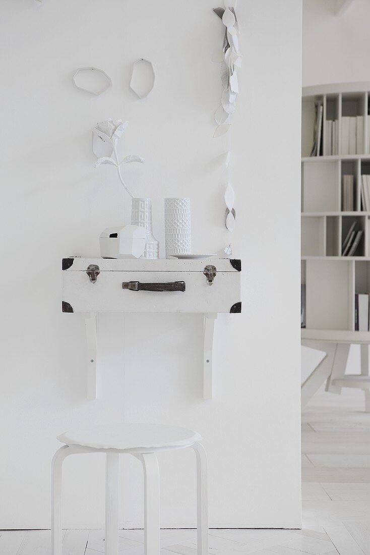 An artistically designed wall with a homemade wall table and a white stool