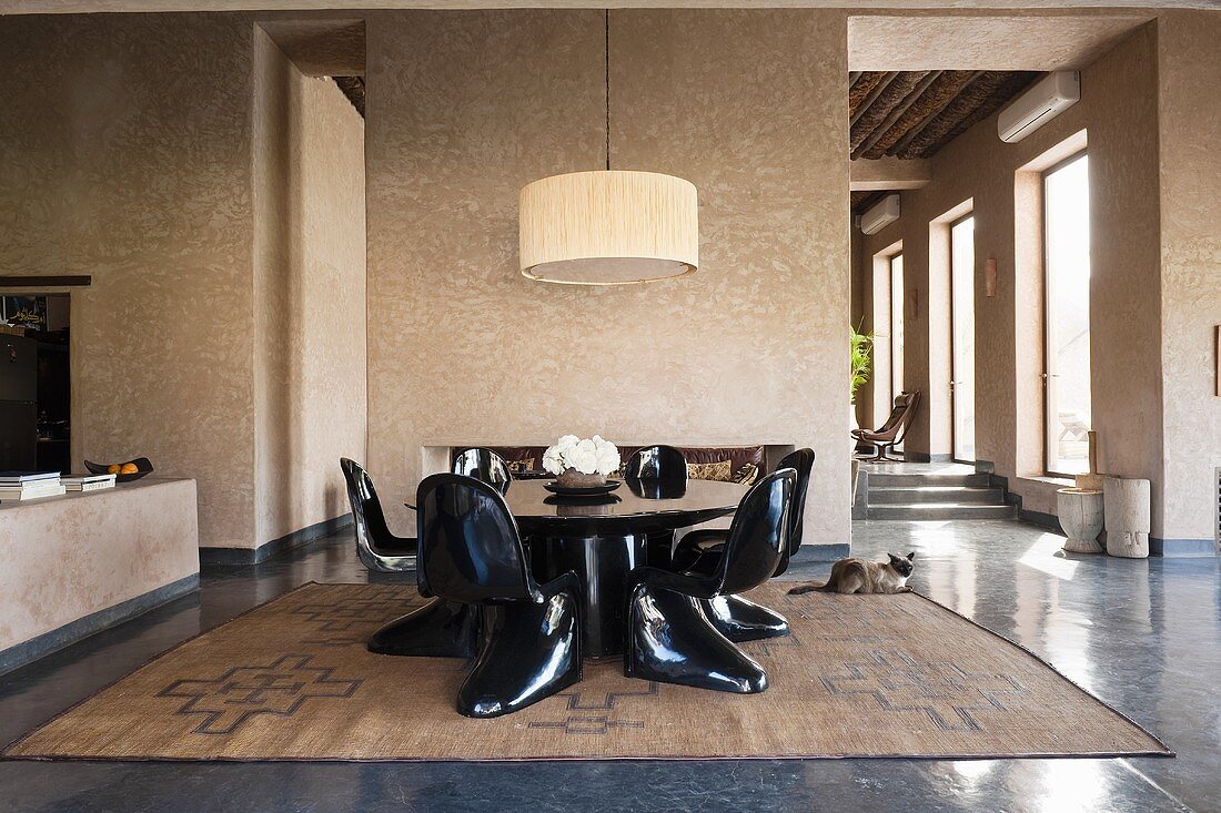 Black plastic chairs around a table with a pendent lamp in front of a wall partition in a Mediterranean country house
