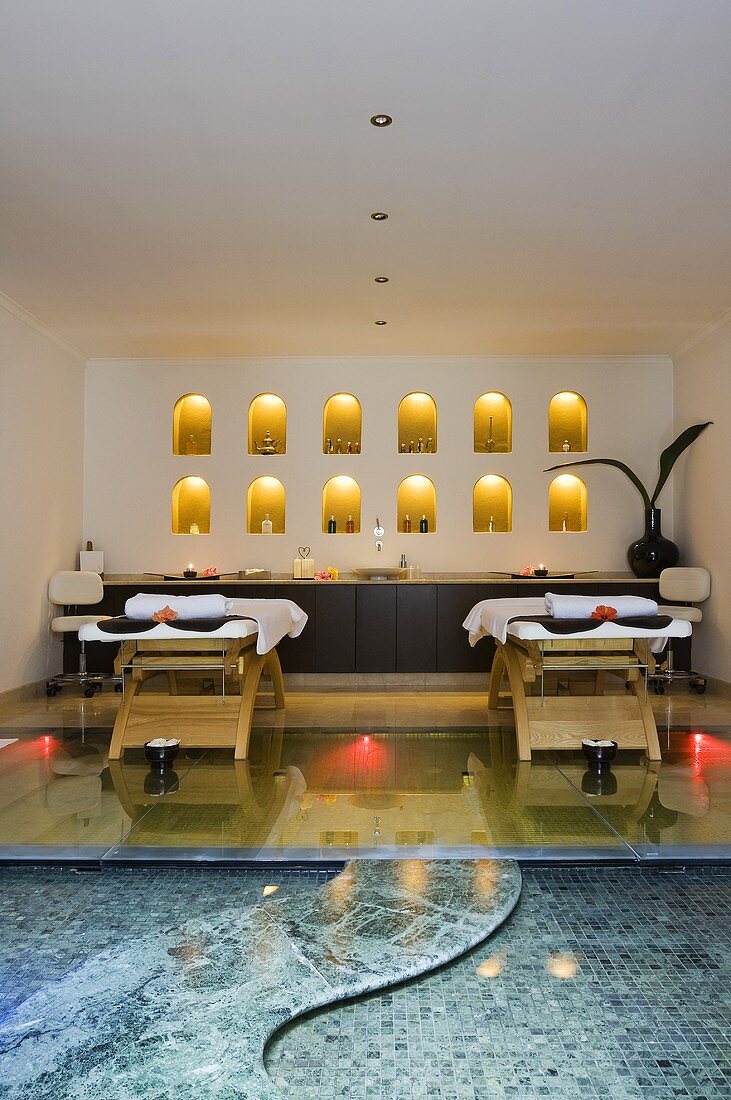 A massage room with a pool - wooden loungers in front of a wall niche and burning candles