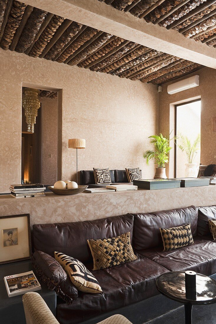 A low sofa with a leather cover and view into a living room with a rustic wood beam ceiling in a Mediterranean house