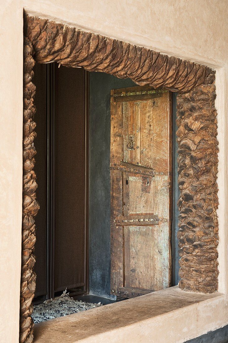 Offener Fensterausschnitt mit rustikalem Natursteinrahmen und Blick auf alte Tür