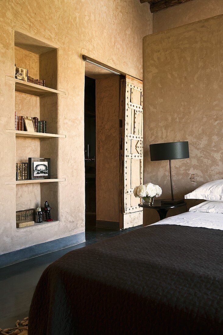 A corner of a bedroom with a shelf in the wall niche and a rustic sliding door